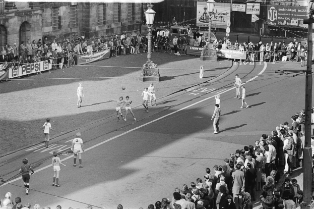 Schwarzes Bild eines Streetsoccer-Spiels mit spielenden Spielern und Zuschauern, einschließlich Bannern und Fenstern in Gebäuden.
