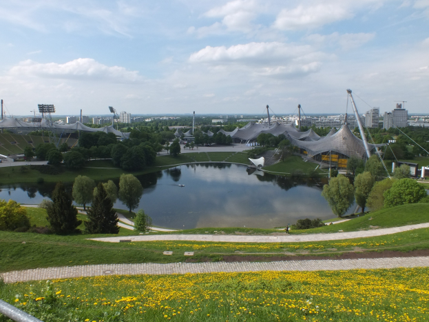 Luftaufnahme des Olympiastadions mit einem Teich, Grünflächen und Gebäuden vor einem klaren Himmel.