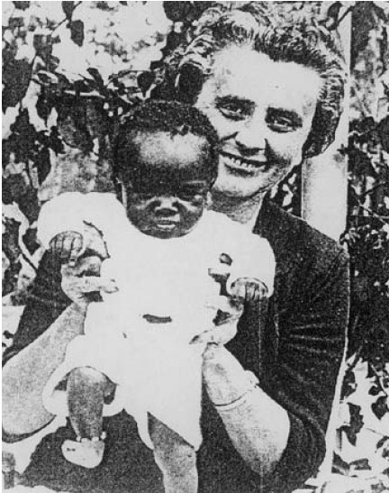 Ein Schwarz-Weiß-Foto einer Frau, die strahlend ein Baby hält, mit Blättern im Hintergrund.