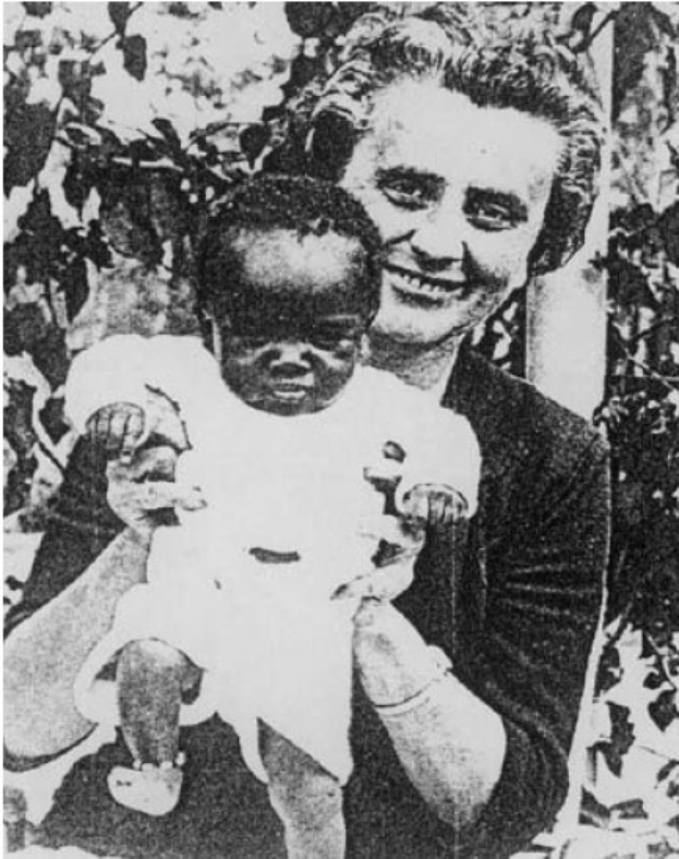 Ein Schwarz-Weiß-Foto einer Frau, die strahlend ein Baby hält, mit Blättern im Hintergrund.