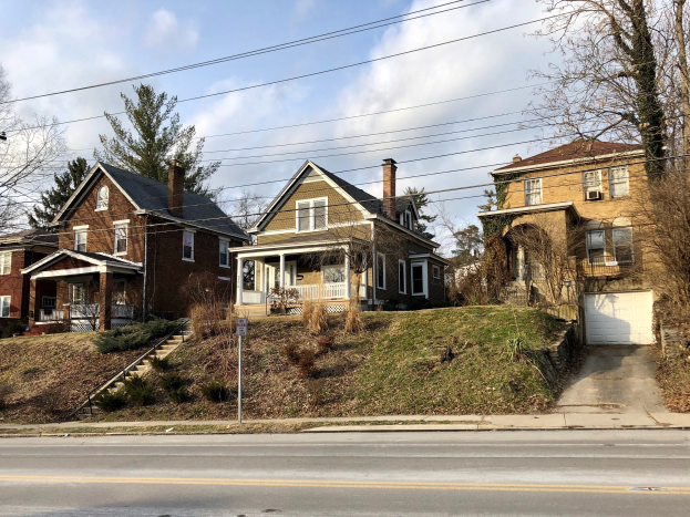 Reihe von Häusern entlang einer Straße mit Fenstern, Türen, Säulen, Geländern, Stufen, Pflanzen, Gras, Bäumen und einem Pfahl mit einer Tafel, die den teuersten Verkauf in Detroit darstellt.