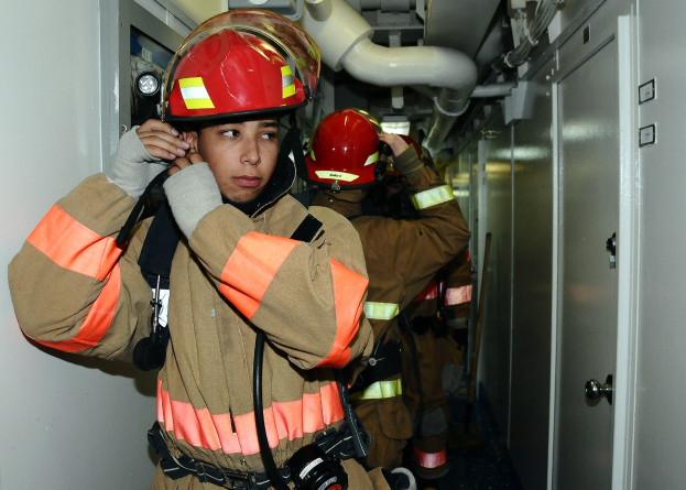 Feuerwehrleute in Uniform, die während einer Übung in einem Raum mit Rohren und Equipment stehen.