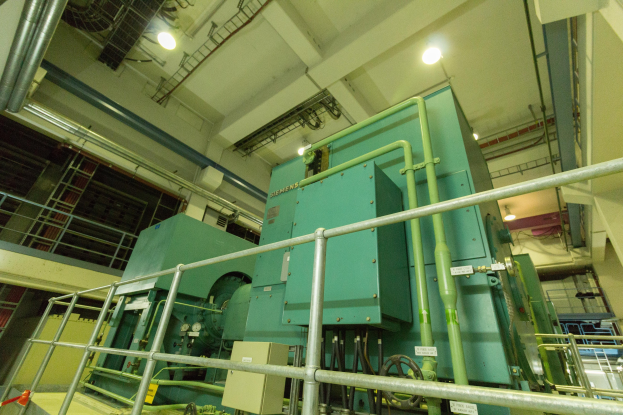 Großes industrielles Wärmeaustauschgerät in einem Gebäude, umgeben von Gelöndern, Rohren, Ventilen und Beleuchtungsausrüstung.
