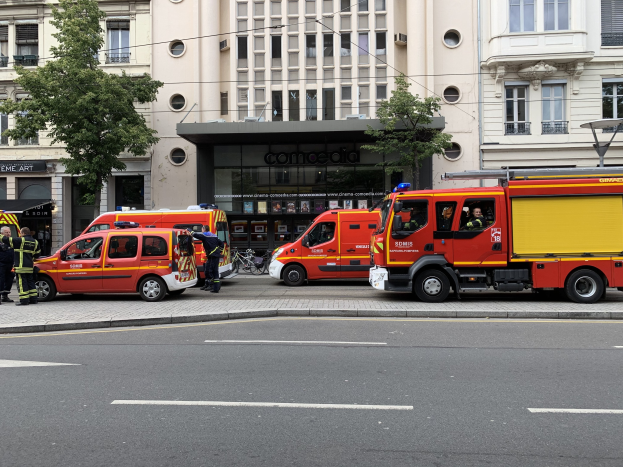 Feuerwehrfahrzeuge auf einer Straße in Paris geparkt, mit Menschen in der Nähe und Gebäuden, Bäumen und einem Fahrrad im Hintergrund.