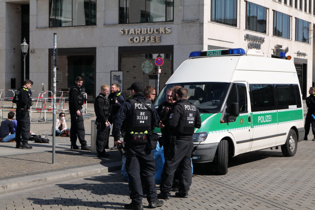 Polizisten vor einem Starbucks-Café mit einem Van auf der rechten Seite und Menschen auf der linken Seite, Hintergrund enthält ein Gebäude, ein Schild, eine Laterne und ein Zaun.