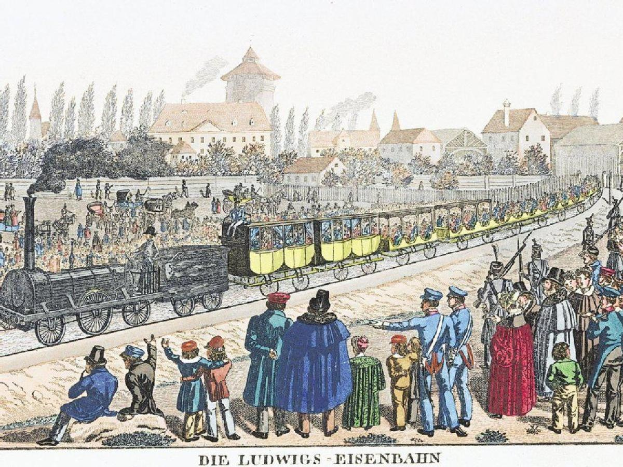 Eine Gruppe von Menschen um einen Zug auf einem Gleis herumstehend, mit einigen im Zug sitzend und anderen auf dem Boden stehend, in der Nähe von Gebäuden und Bäumen, mit Text unten lesend "Ludwigs-Eisenbahn, die erste Bahnstation in Deutschland"