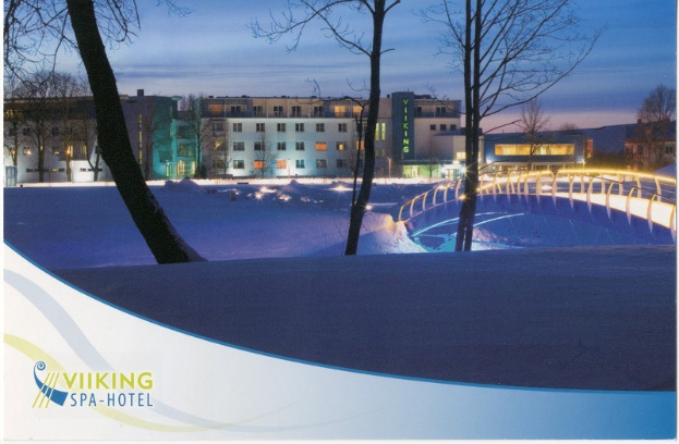 Winterszene eines Wikinger-Spa-Hotels mit schneebedeckter Erde, einer beleuchteten Brücke, Bäumen, Gebäuden mit Fenstern und einem bewölkten Himmel; Text ist auf der linken Seite sichtbar.