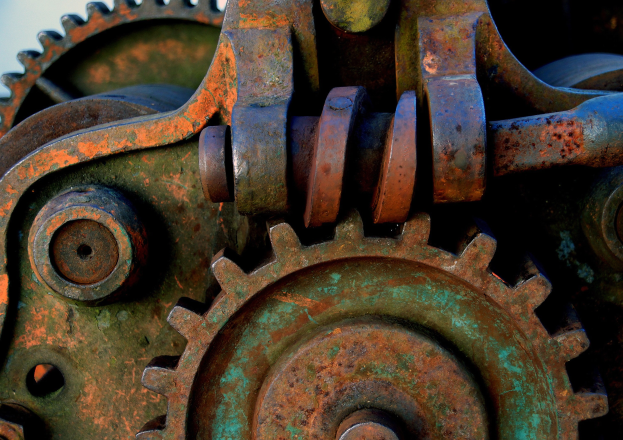 Nahaufnahme eines verrosteten Metallzahnrades mit mehreren Zähnen und Zahnrädern, das starke Abnutzung und Korrosion zeigt.