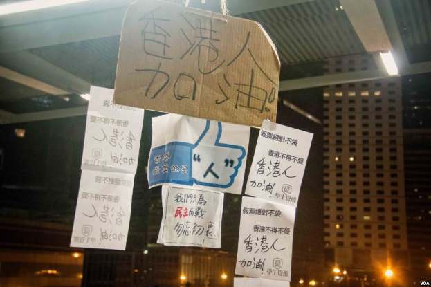 Menschen stehen vor einem Gebäude in der Nacht mit beleuchteten Protestschildern an der Decke.