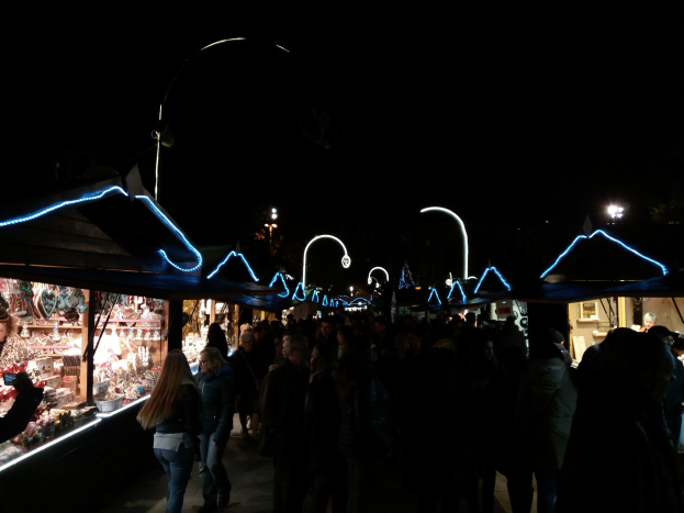 Eine Menschenmenge, die nachts eine Straße entlanggeht, gesäumt von beleuchteten Ständen mit verschiedenen Artikeln, die eine festliche Atmosphäre schaffen.